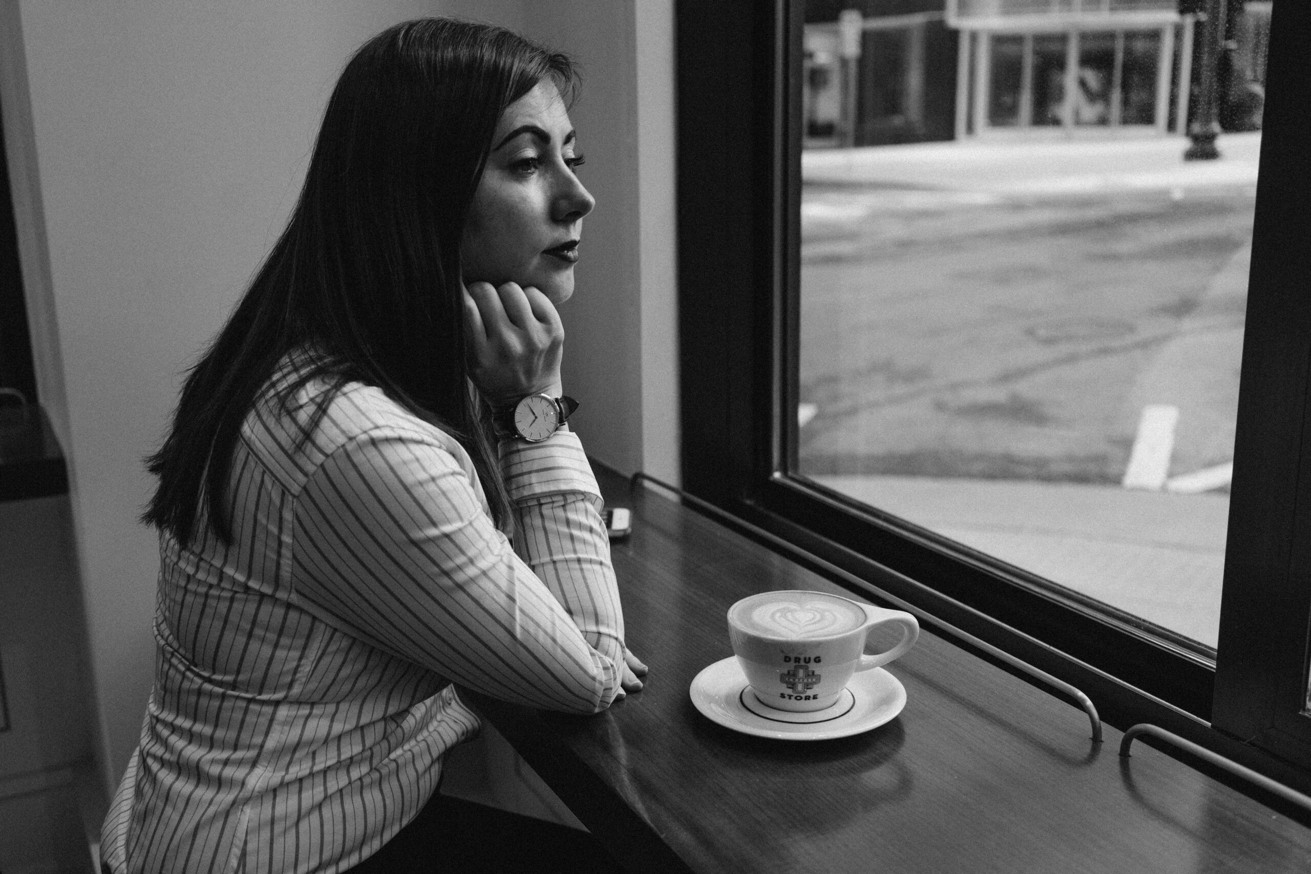 Woman in profile looking thoughtfully out a window with a coffee — representing the quiet questioning many people experience when concussion symptoms are misdiagnosed as anxiety or depression.